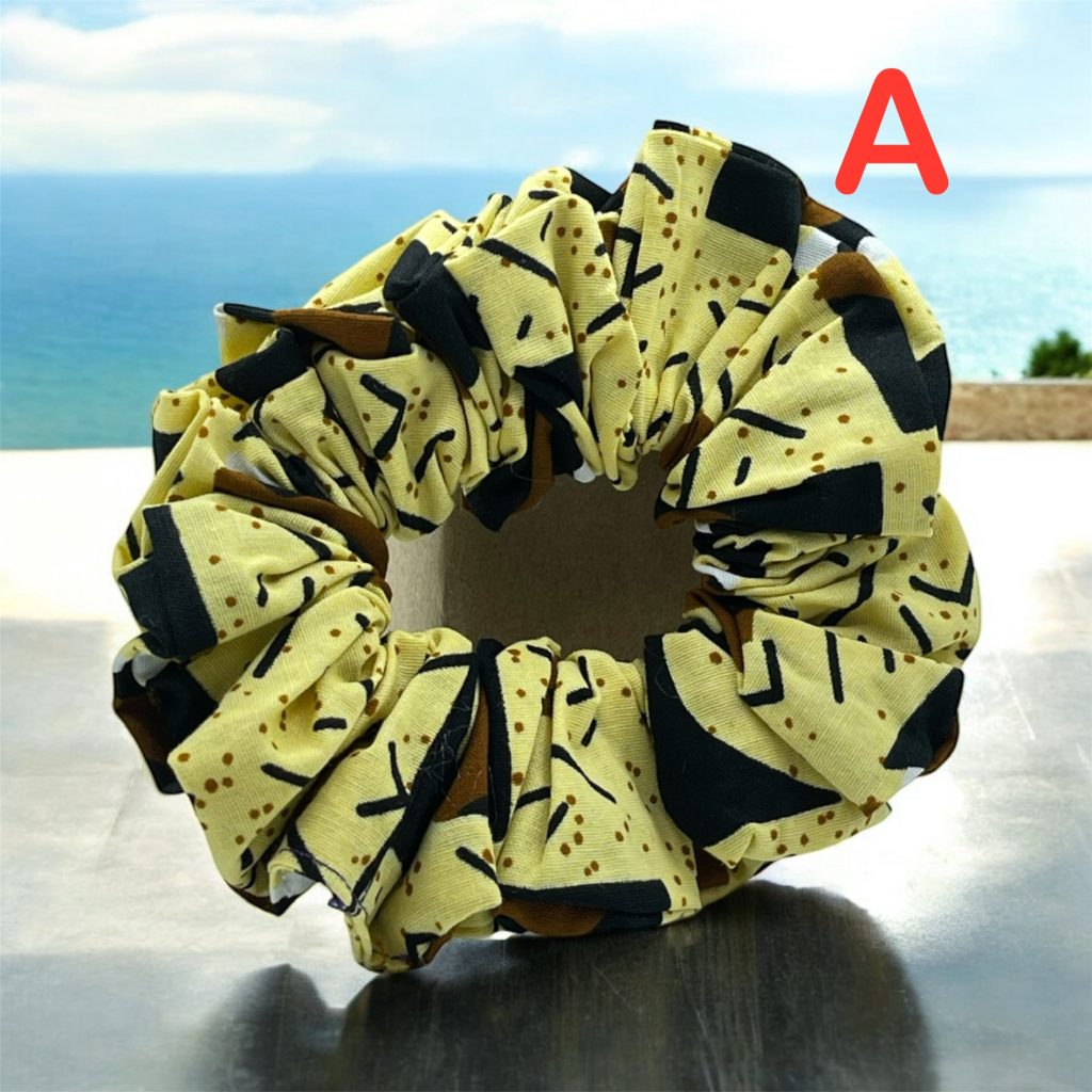 Yellow fabric scrunchies for the hair with black and brown geometric patterns, placed on a table with the sea in the background.