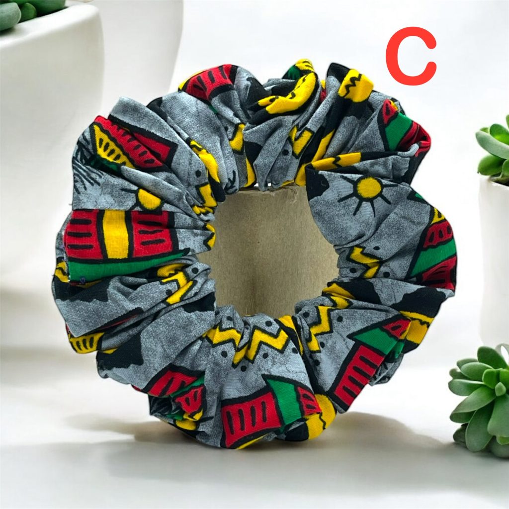 Gray scrunchies for the hair with red, yellow, green, black, and white patterns, placed on a table with plants in the background.