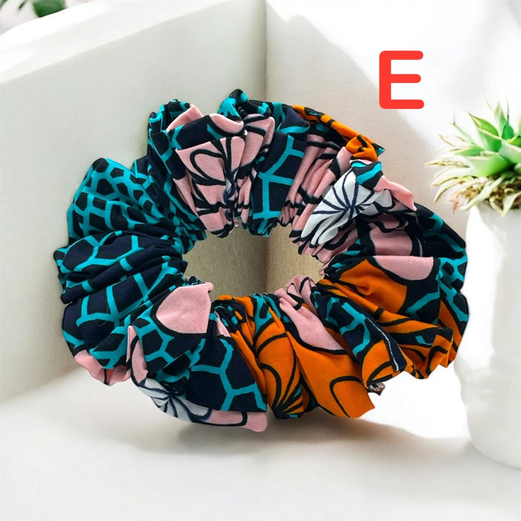 Scrunchies for the hair in teal, orange, pink, black, and white patterns with bold abstract designs, placed on a light background with plants.