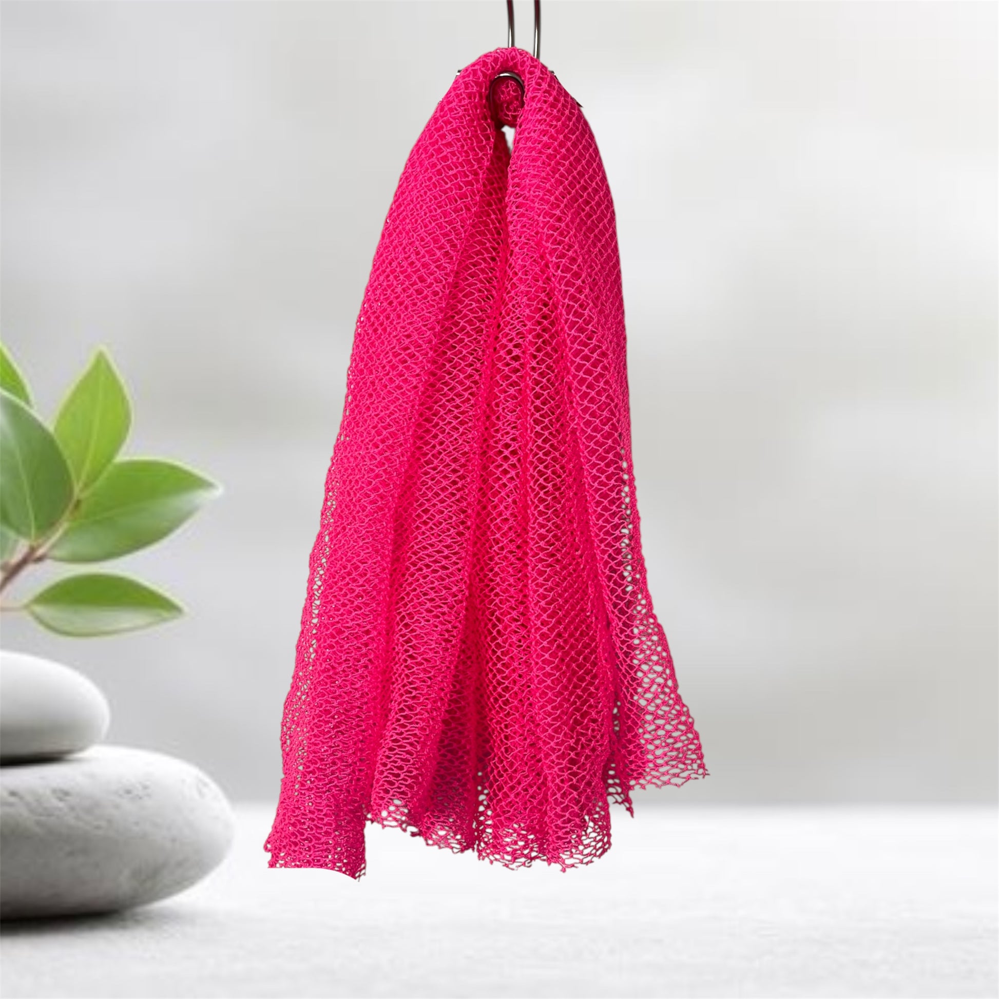 Pink mesh scrubber hanging on a hook with a plant and stones in the background