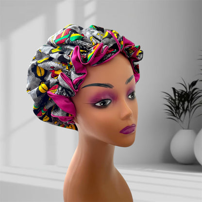 A mannequin head wearing a stylish hair bonnet with a vibrant abstract pattern, featuring colors gray, pink, yellow, green, red, and black, set against a blurred indoor background with potted plants.