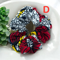 Scrunchies for the hair in white, black, red, and yellow patterns with bold abstract designs, placed on a light background near green plants.