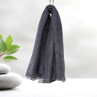 Grey mesh scrubber hanging on a hook with a plant and stones in the background