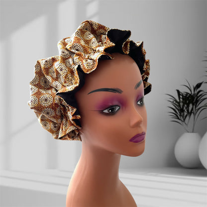 A mannequin head wearing a stylish hair bonnet with a geometric circular pattern, featuring colors gold, black, white, and brown, set against a blurred indoor background with potted plants.
