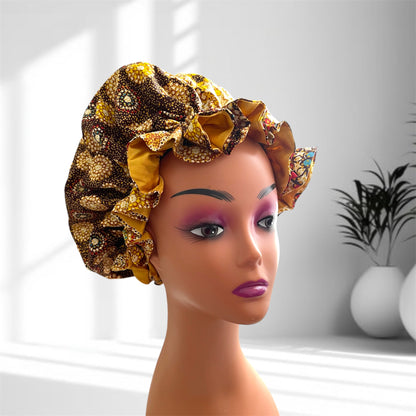 Stylish hair bonnet with a golden yellow, brown, and black patterned fabric, featuring small white and green accents, displayed on a mannequin head in a softly lit indoor setting.