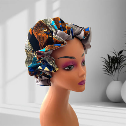 "A mannequin head wearing a stylish hair bonnet with an abstract pattern, featuring colors black, orange, blue, yellow, and gray, set against a blurred indoor background with potted plants."